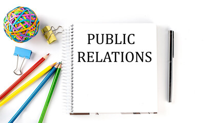 Notebook ,pencils,pen and rubber band with text PUBLIC RELATIONS on the white background