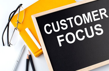 CUSTOMER FOCUS text on the blackboard with notepad , pen, pencil