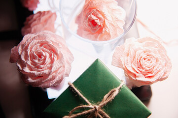 Pink roses handmade from paper next to a green gift box. View from above. Selective focus. Copy space