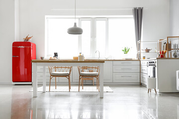 Interior of light modern kitchen with red fridge, white counters and dining table
