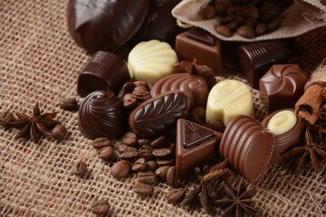 Assortment of dark, white and milk chocolate sweets, zefir (zephyr). Chocolate and coffee beans on rustic wooden sacking background. Spices, cinnamon. Chocolates background.