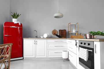 Interior of light modern kitchen with red fridge and white counters