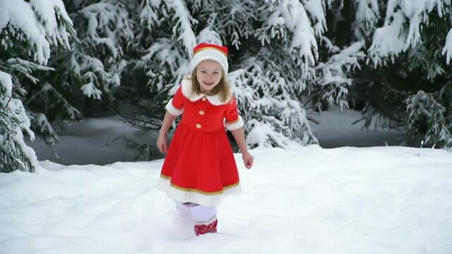Happy christmas girl smille in santa costume in snow. Winter forest with snowdrifts and snacks. child laughs at new year and walks outside. red suit hat. Dance have fun. Portrait laughing childhood.