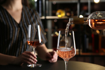 Pouring rose wine from bottle into glass indoors, closeup. Space for text