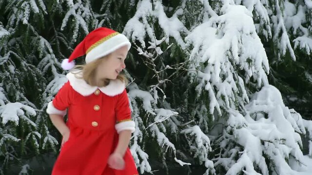 Happy christmas girl smille in santa costume in snow. Winter forest with snowdrifts and snacks. child laughs at new year and walks outside. red suit hat. Dance have fun. Portrait laughing childhood.