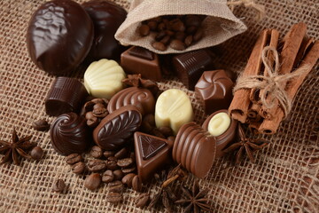 Assortment of dark, white and milk chocolate sweets, zefir (zephyr). Chocolate and coffee beans on rustic wooden sacking background. Spices, cinnamon. Chocolates background.