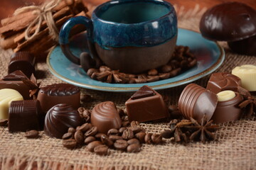 Coffee cup, beans, chocolate on old kitchen table Assortment of dark, white and milk chocolate sweets, zefir (zephyr). Spices, cinnamon.