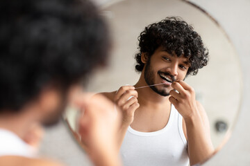 Toothcare concept. Bearded indian man using teeth floss caring for oral hygiene and dental health