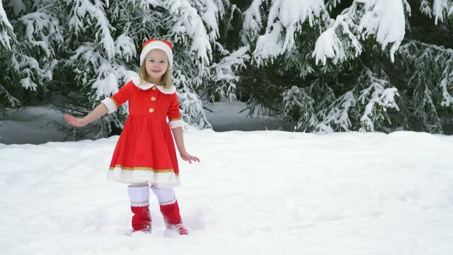 Happy christmas girl smille in santa costume in snow. Winter forest with snowdrifts and snacks. child laughs at new year and walks outside. red suit hat. Dance have fun. Portrait laughing childhood.