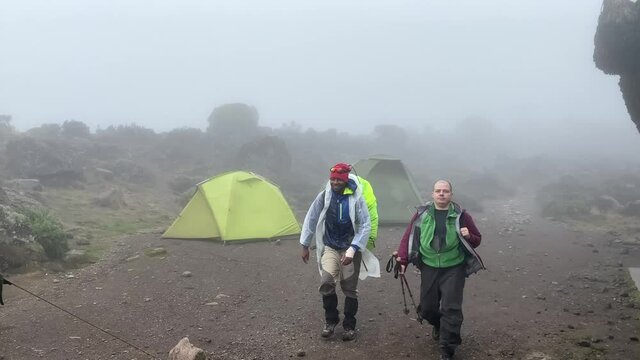 A white male tourist walks with his black guide to the Baranco camp. Climbing Kilimanjaro in December, Tanzania, Africa. Foggy mountain landscape.