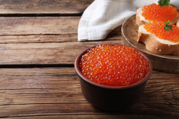 Bowl with delicious red caviar on wooden table. Space for text