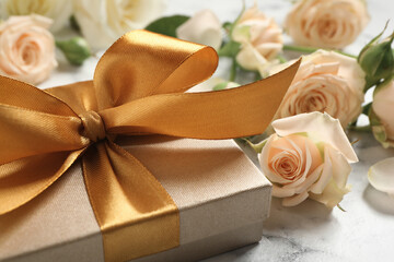 Golden gift box and beautiful roses on white marble table, closeup