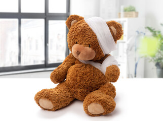 medicine, healthcare and childhood concept - teddy bear toy with bandaged head and paw over medical office at hospital background
