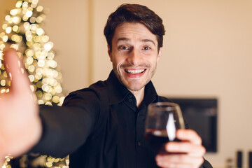 Young man drinking red wine, looking at camera