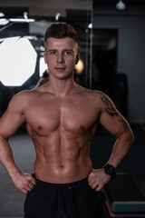 Fototapeta na wymiar Muscular sporty young man with hairstyle and naked strong body posing in the gym and looking at the camera