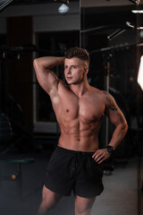 Fototapeta na wymiar handsome sports young man model with a slender muscular naked torso poses and trains in the gym