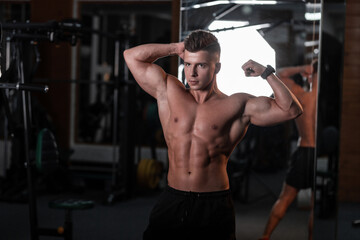 Fototapeta na wymiar handsome young bodybuilder guy with a naked tanned torso trains in the sports gym