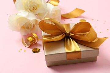 Beautiful golden gift box, flowers and confetti on pink background