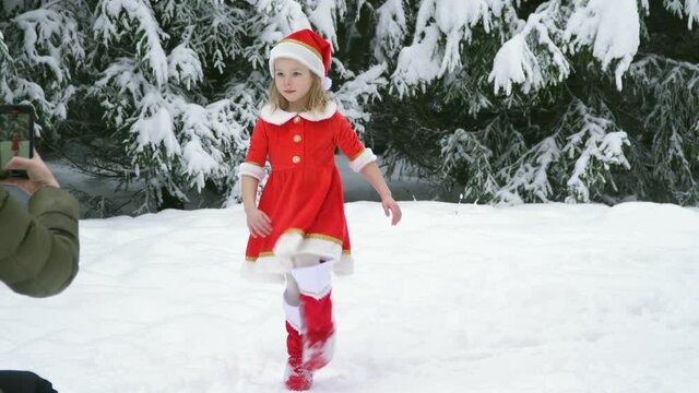 Happy christmas girl smille in santa costume in snow. Winter forest with snowdrifts and snacks. child laughs at new year and walks outside. red suit hat. Dance have fun. Portrait laughing childhood.