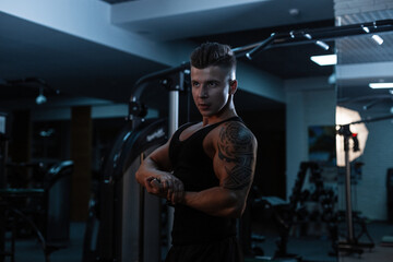 Fototapeta na wymiar Handsome young sports man with a muscular body with tattoo in a sports black T-shirt with shorts shows muscles in the gym