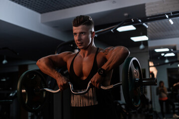 Fototapeta na wymiar Handsome strong man trainer with a muscular body pumps muscles in the gym against a dark background