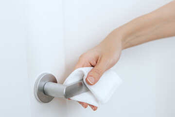 Cleaning door handles with an antiseptic wet wipe and gloves. Sanitize surfaces prevention in hospital and public spaces against corona virus. Woman hand using towel for cleaning home room door link.