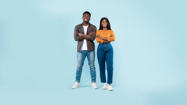 Confident couple standing with folded arms at blue studio background