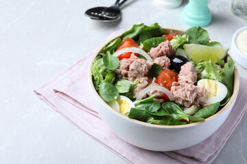 Bowl of delicious salad with canned tuna and vegetables on light table, space for text
