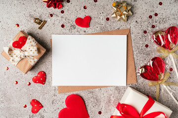 Flat lay of paper envelope with blank mockup greeting card. Grey table background with Valentine day gift, letter, heart shape, confetti, lollipops and decoration. Top view, mock up invitations