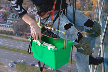 worker in climbing gear with a green bucket washes the mirror glazing of the facade of the building