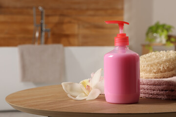 Dispenser of liquid soap and orchid flower on wooden table in bathroom, space for text