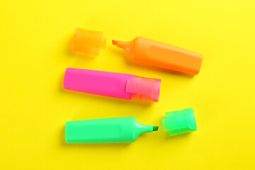 Colorful markers on yellow background, flat lay. School stationery