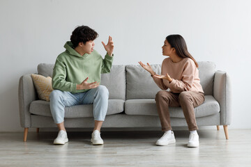 Breakup and divorce concept. Young married Asian couple having fight, yelling at each other in living room - obrazy, fototapety, plakaty