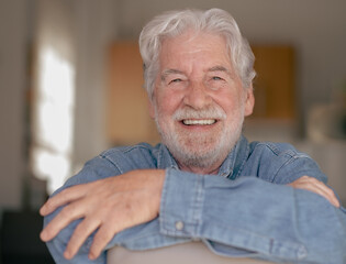Portrait of beautiful senior bearded man smiling sitting at home with crossed arms. Relaxed caucasian grandfather posing for photography looking at camera