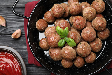 Tasty cooked meatballs with basil on black wooden table, flat lay