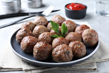 Tasty cooked meatballs with parsley on light grey table, closeup
