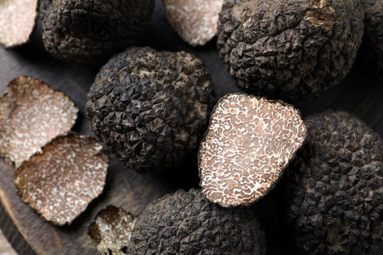 Whole and cut black truffles on wooden board, top view