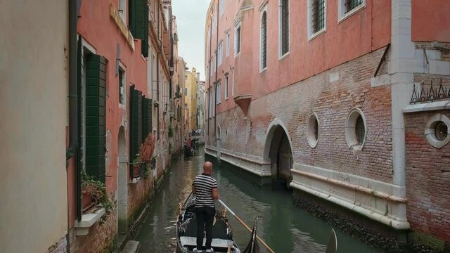 Gondola go down canal at day, Venice, Italy. Gondolier navigate boat. Tourists enjoy ride and take photos. Medieval buildings, channel waters 