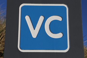 A close up view of a blue and white sign with VC lettering indicating a visitor centre in Wales, UK.