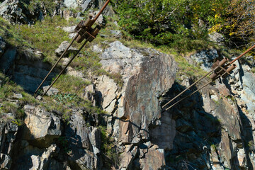 Close-up fastening of metal cables, structures into the rock on a sunny day. Metal fastening of a suspension bridge across a river in a rock or mountain