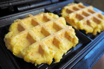 front view of two fresh Belgian waffles made from cornmeal, eggs and pumpkin, lying in a waffle iron during cooking