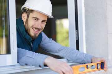 happy worker inspecting a window sill using a builders level