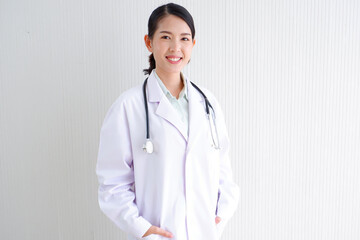 Smiling Asian female doctor puts a stethoscope on her shoulder. wearing white lab coat on gray background.