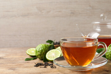 Glass cup of tasty bergamot tea and fresh fruits on wooden table, space for text