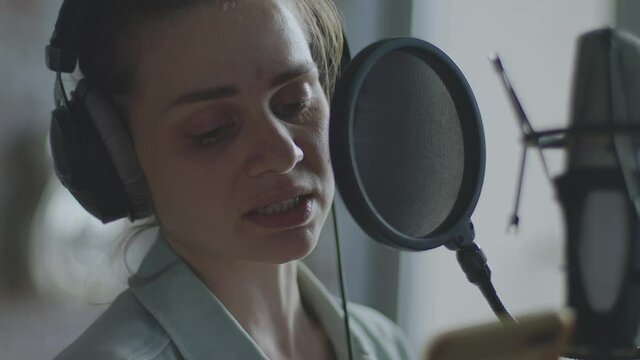 A young girl in monitor headphones in front of a microphone records a podcast