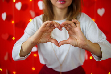 A girl in a white blouse shows a heart with her hands. Red background. Valentine's day concept