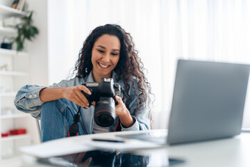 Female Photographer Holding Camera Looking At Photos Using Laptop Indoors