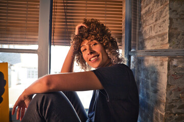 Beautiful woman sitting on the edge of a large window in her studio while making different...
