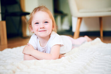 Fototapeta premium Cute little girl lying on the floor at home and smile