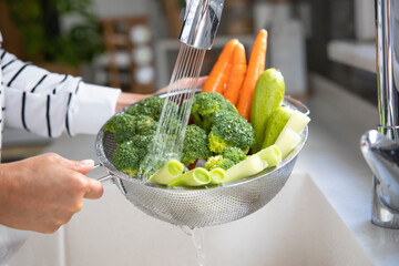 Woman washing vegetables on kitchen counter.